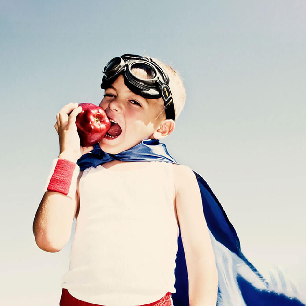 Junge beißt in einen roten Apfel und trägt ein Superman Kostüm