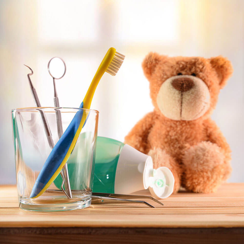 Zahnputzutensilien im Becher mit einem Teddybär daneben